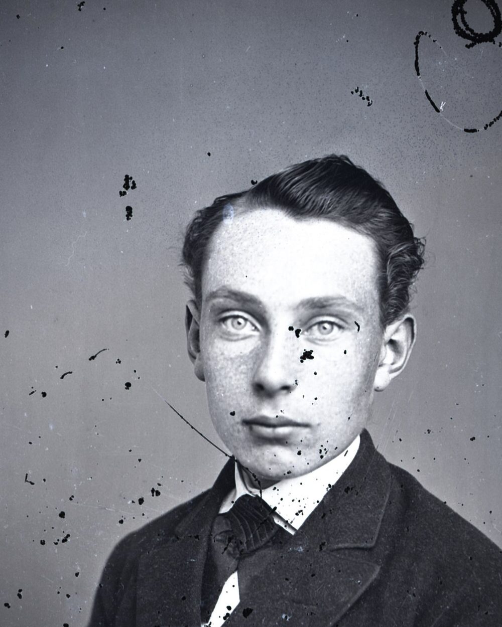 A glass negative portrait of a young man covered in black spots and scratches.